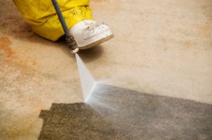 A professional worker pressure washing the floor of an apartment.
